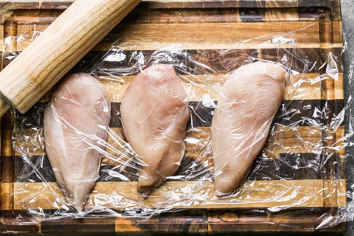 Raw chicken breasts in plastic wrap on a cutting board