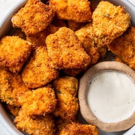 A bowl of crispy, golden-brown air fryer chicken nuggets with a side of creamy dipping sauce.