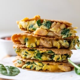 Stacked breakfast quesadillas filled with spinach, scrambled eggs, and beans on a wooden board, with a bowl in the background.
