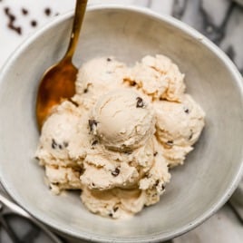 A bowl of creamy cottage cheese ice cream with chocolate chips, served with a gold spoon on a marble surface.