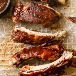 Instant Pot ribs coated in a rich, glossy sauce are arranged on a wire rack over parchment paper, with a small bowl of extra barbecue sauce in the corner.