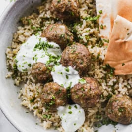 Baked lamb meatballs in bowl with rice, tzatziki, and pita bread