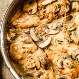 Mushroom chicken in a creamy sauce, garnished with fresh herbs, cooked in a skillet on a wooden surface.