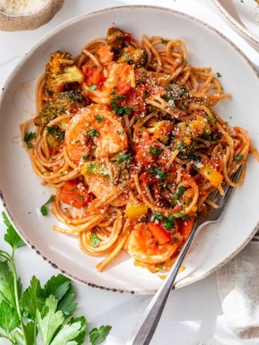 A plate of spicy shrimp pasta with tomato sauce, shrimp, broccoli, bell peppers, and parsley, with a fork on the plate.