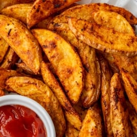 A plate of golden-brown steak fries seasoned with spices, served with a small dish of ketchup on the side.