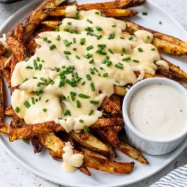 Plate of voodoo fries topped with melted cheese and chopped chives, served with a cup of creamy dipping sauce.