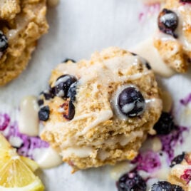 Lemon blueberry biscuits cooling on parchment paper and topped with glaze