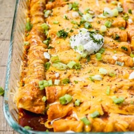 Cheesy ground beef enchiladas topped with sour cream, chopped green onions, and herbs in a glass baking dish.