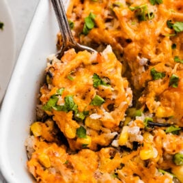 A spoon serving chicken and rice casserole from a baking dish