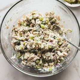 A glass bowl filled with creamy chicken salad mixed with chopped celery, red onion, and dill pickles