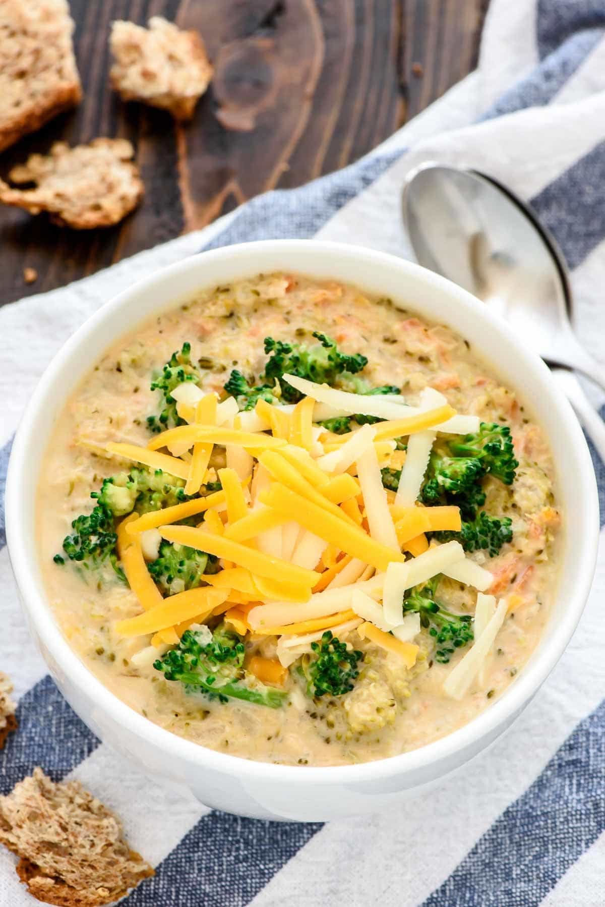 white bowl of Crockpot Broccoli Cheese Soup garnished with shredded cheddar cheese