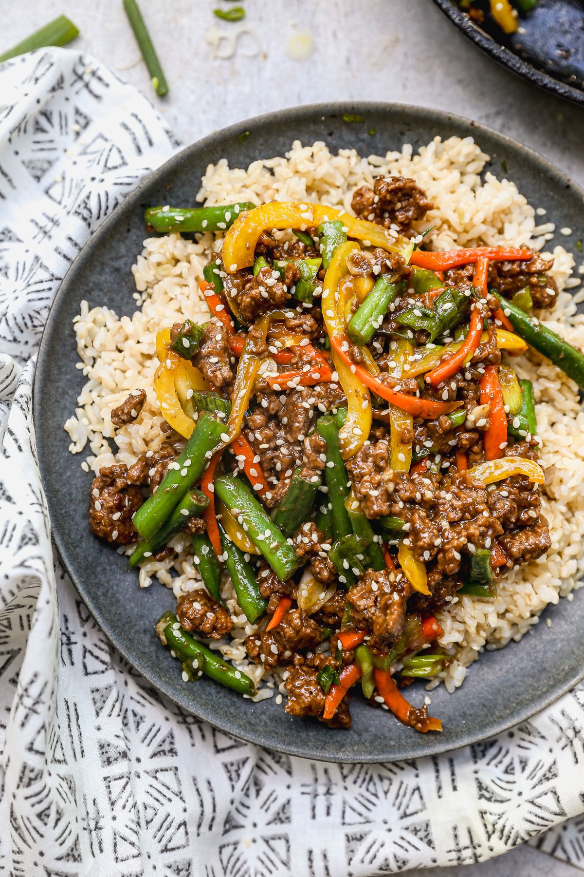 A plate of brown rice topped with ground beef stir fry, served on a patterned cloth.