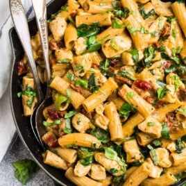 Cheesy Tuscan chicken macaroni and cheese in a skillet with two silver spoons