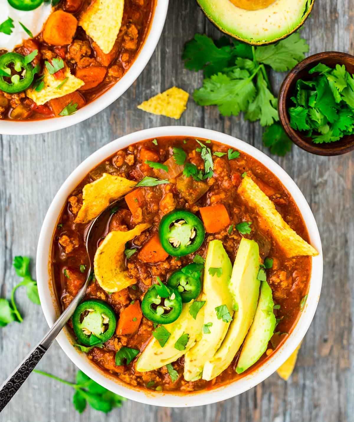The BEST Healthy Turkey Chili. — Only 227 calories and 24 g. protein per serving! Hearty, warm, filling with the perfect amount of spice. This simple recipe will be your new chili go-to! Made with sweet potatoes and no beans, it's filled with vegetables, low carb, and cooked on the stovetop until it's thick and rich. #wellplated #turkeychili #healthy Healthy turkey chili served in a bowl with tortilla chips, avocado, and jalapenos