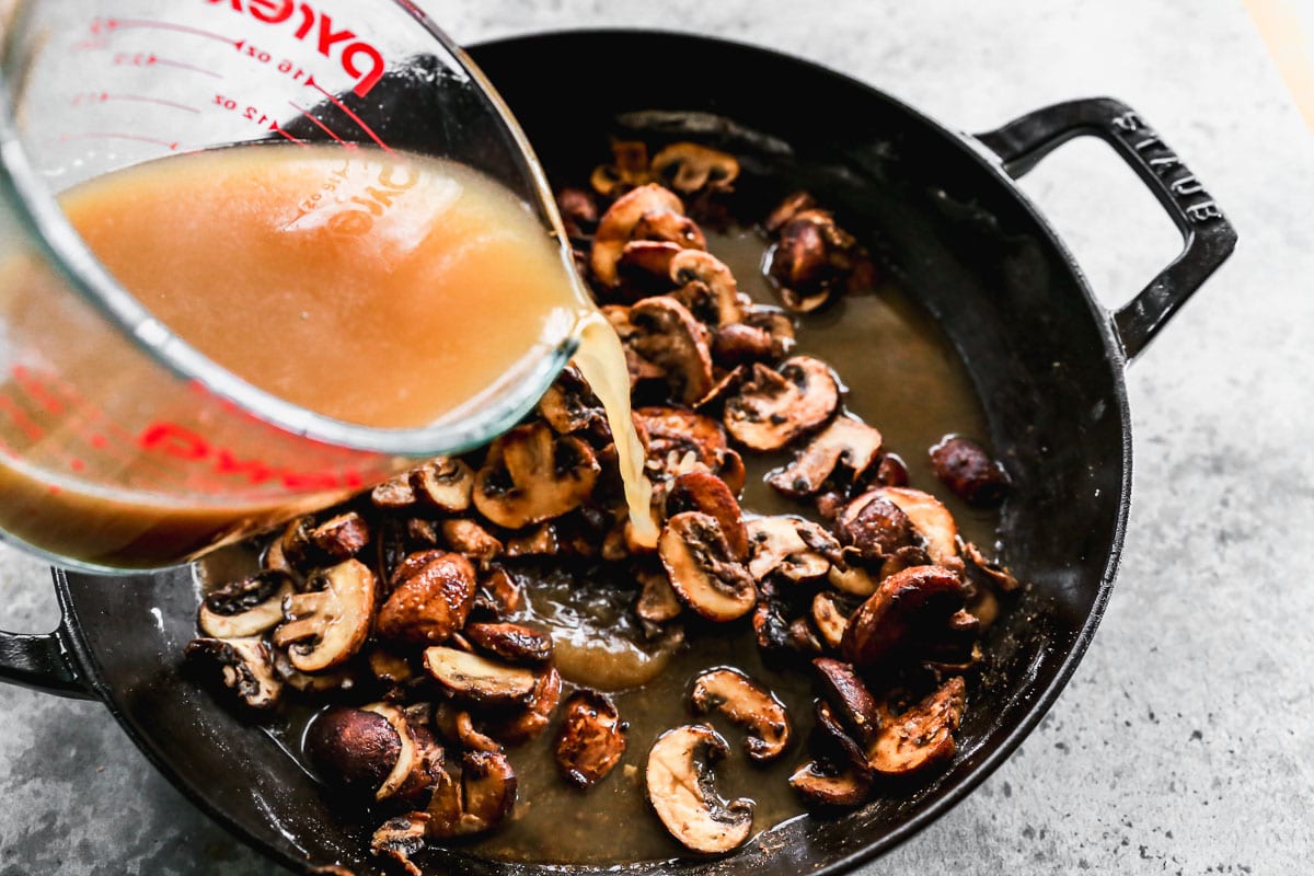 adding broth to a pan of browning mushrooms for traditional beef stroganoff