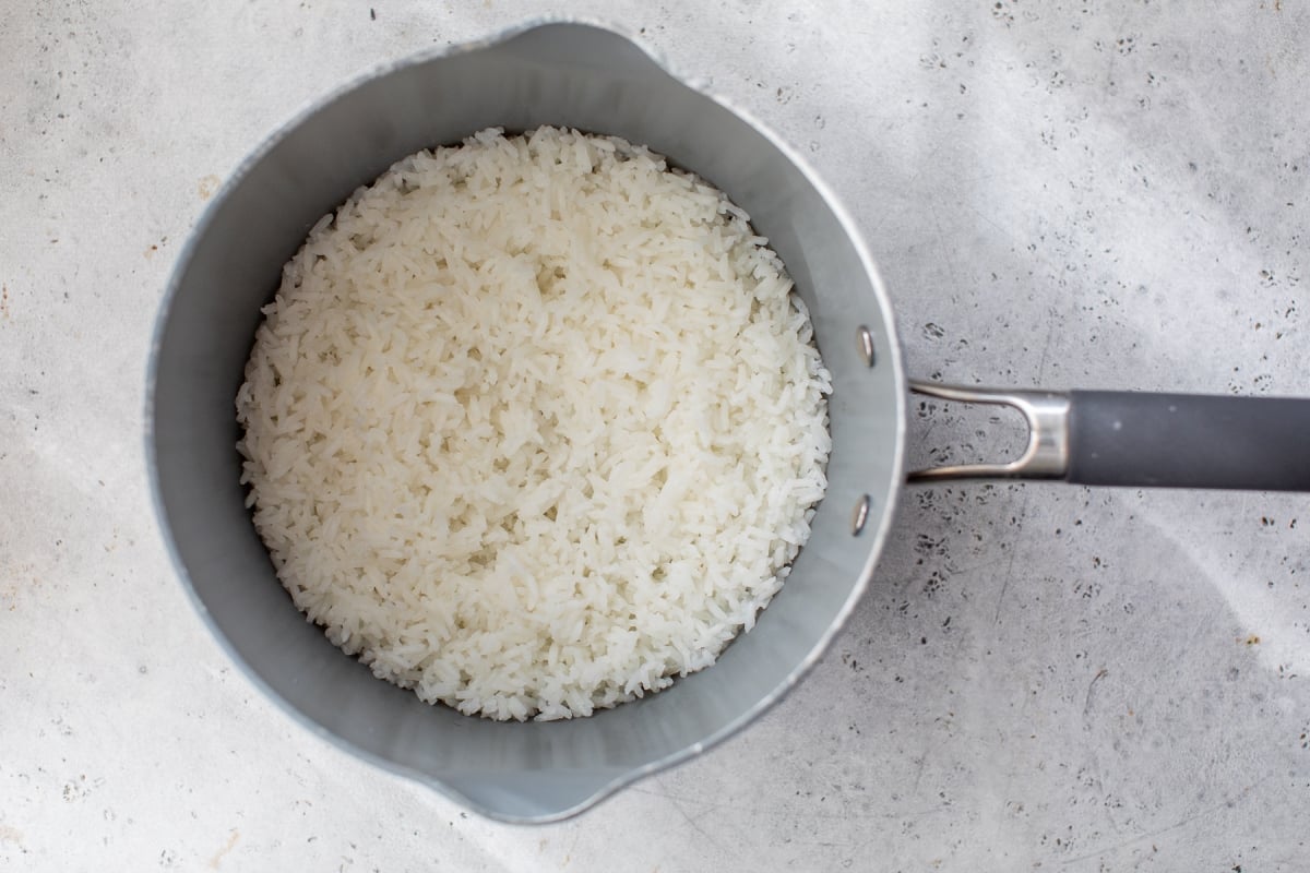 A pot filled with freshly cooked white rice sits on a light gray textured surface, viewed from above.