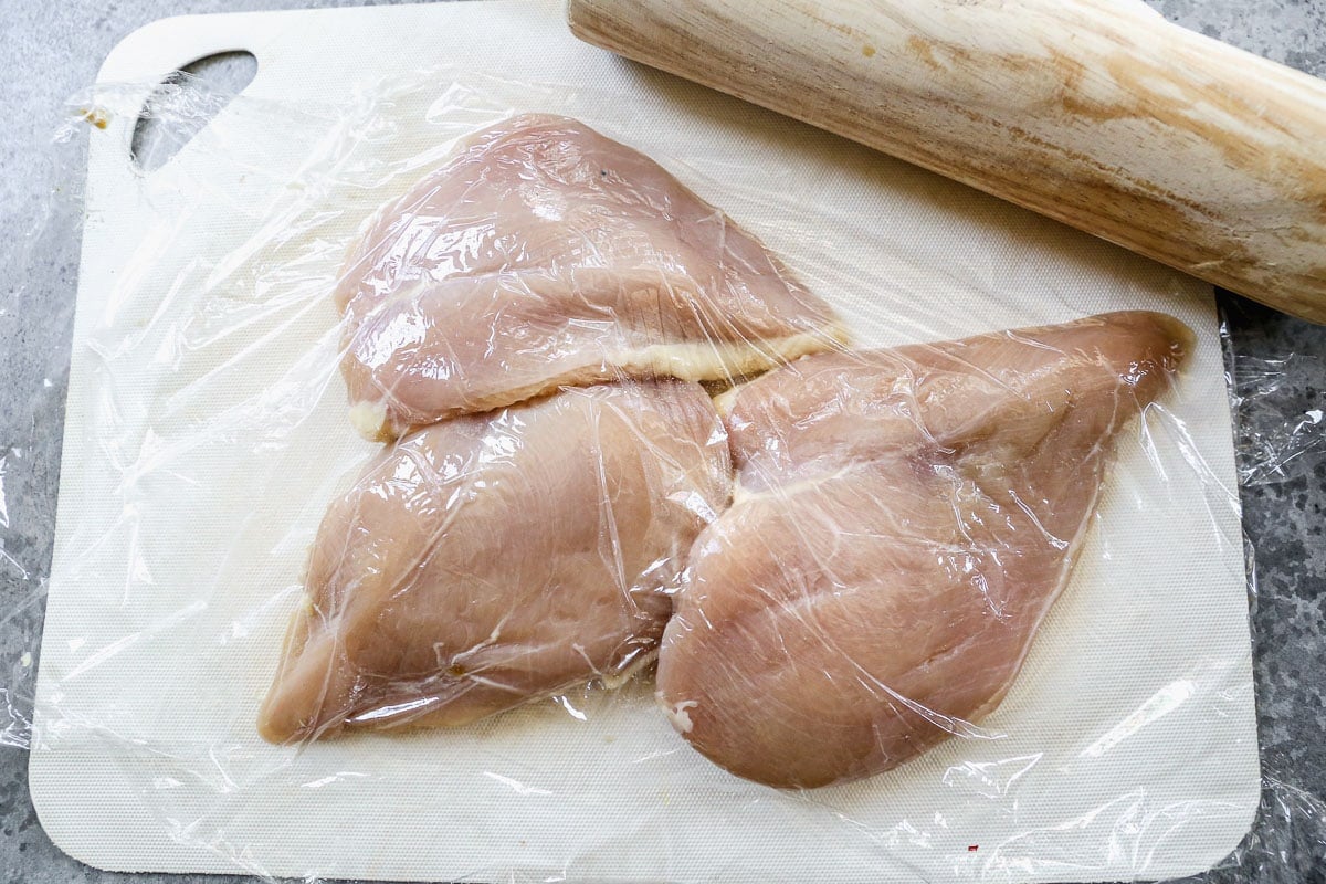 Three raw chicken breasts under plastic wrap