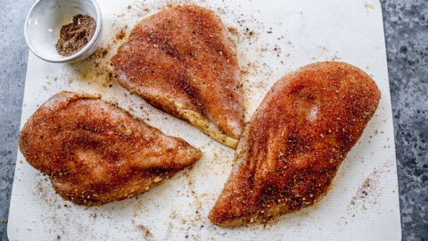 Three raw chicken breasts with seasonings