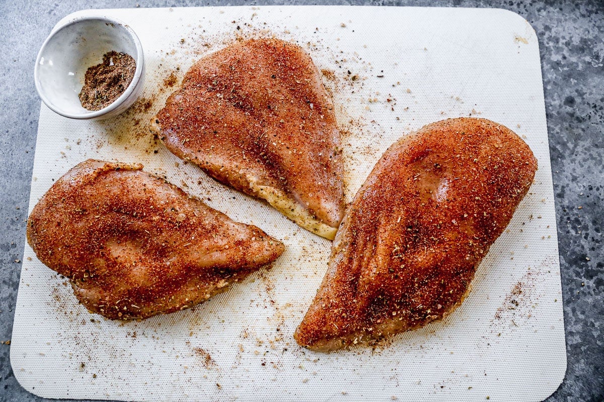 Three raw chicken breasts with seasonings