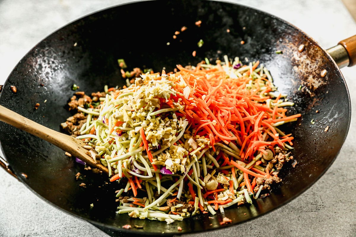 adding grated carrots and broccoli slaw to a wok of seasoned ground turkey and vegetables