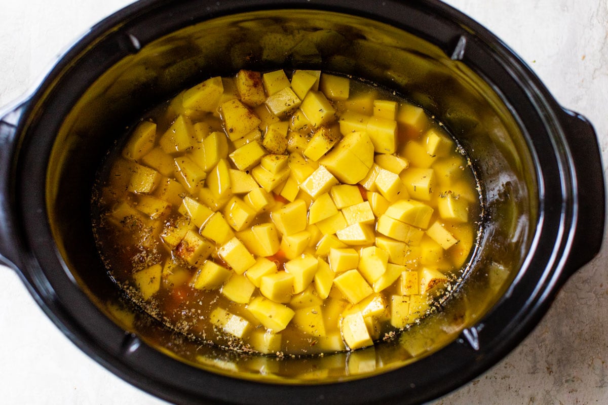 cubed potatoes, herbs, carrots, and chicken broth in a slow cooker
