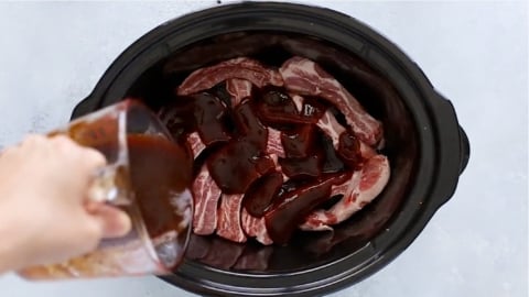 pouring sauce over pork ribs in a crock pot