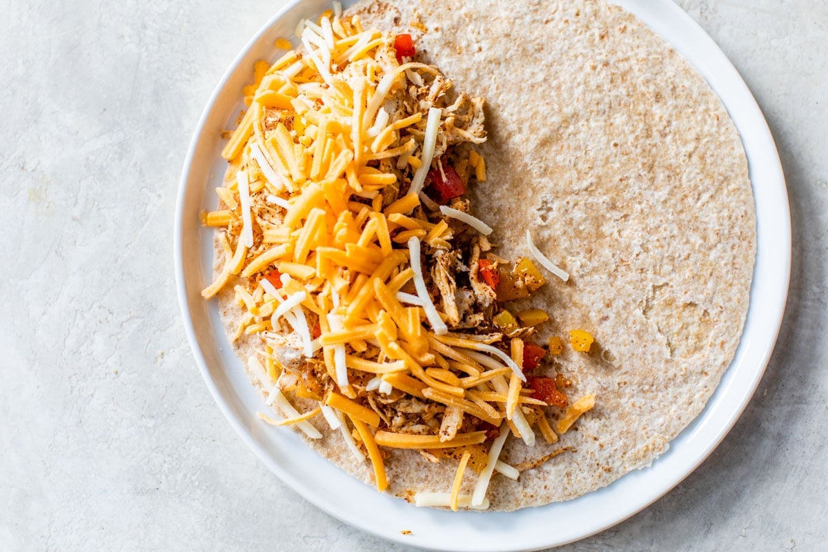 A tortilla with cheese, chicken, and vegetables on a plate