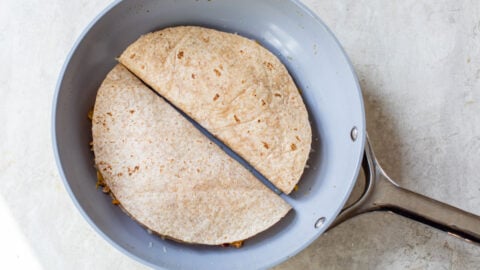 Two tortillas with cheese and meat in a skillet