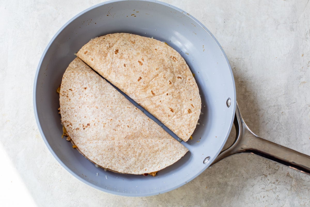Two tortillas with cheese and meat in a skillet