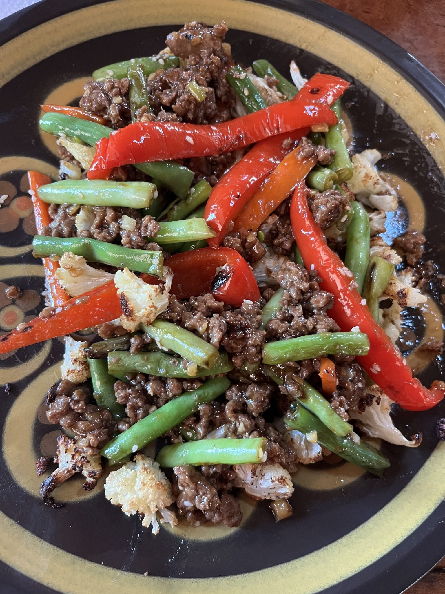 A colorful plate of stir-fried ground beef with green beans, red bell peppers, and cauliflower, served on a decorative yellow and black plate.