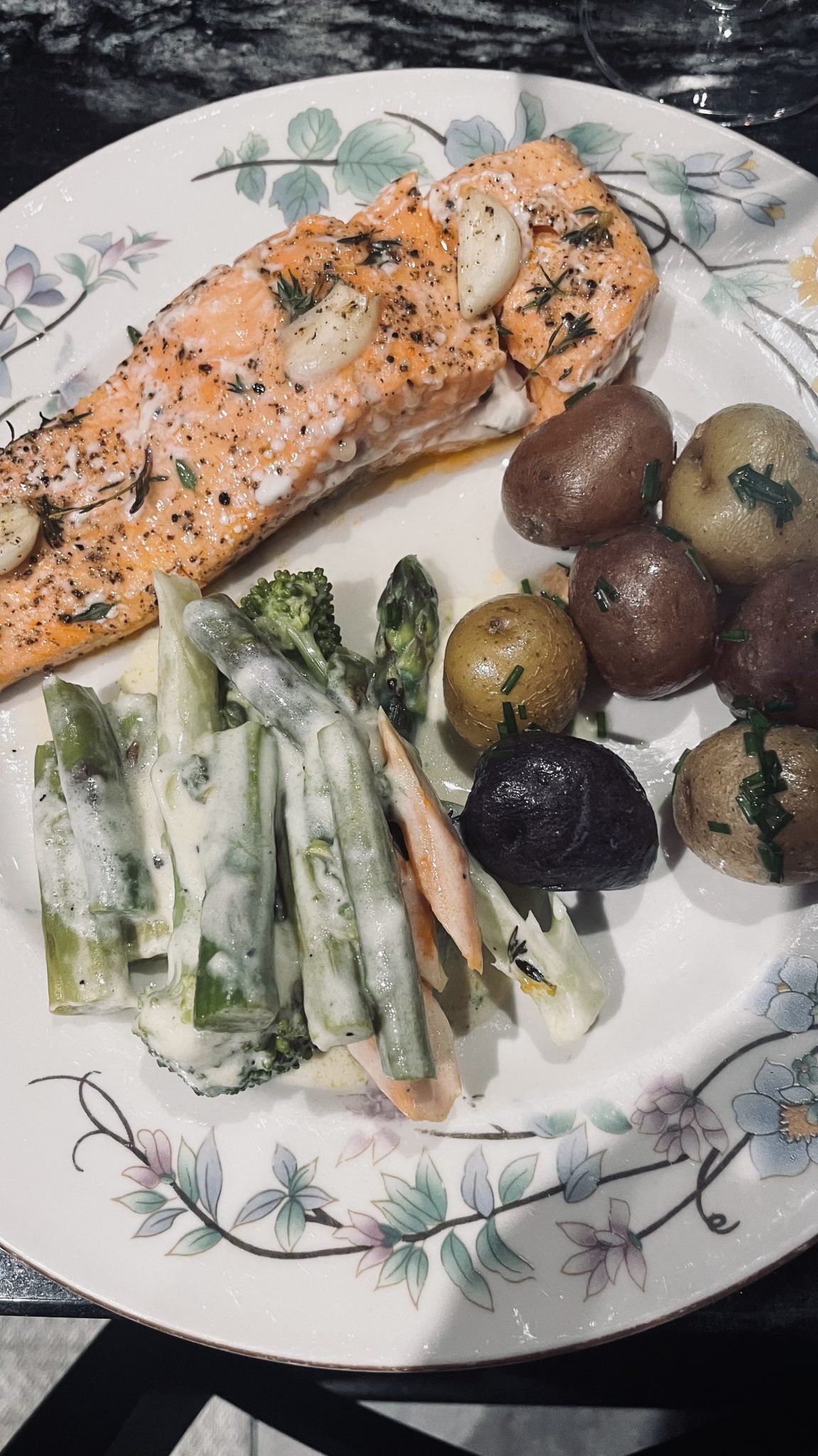 A plate with baked salmon topped with herbs and garlic, roasted potatoes, and creamy mixed vegetables.