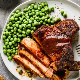 An air fryer pork chop on a plate with peas