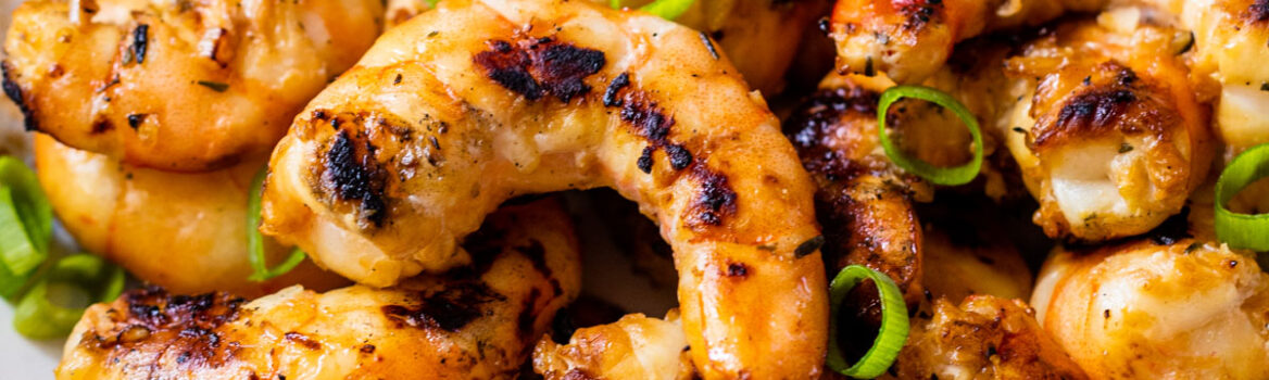 Grilled shrimp garnished with chopped green onions served on a white plate.